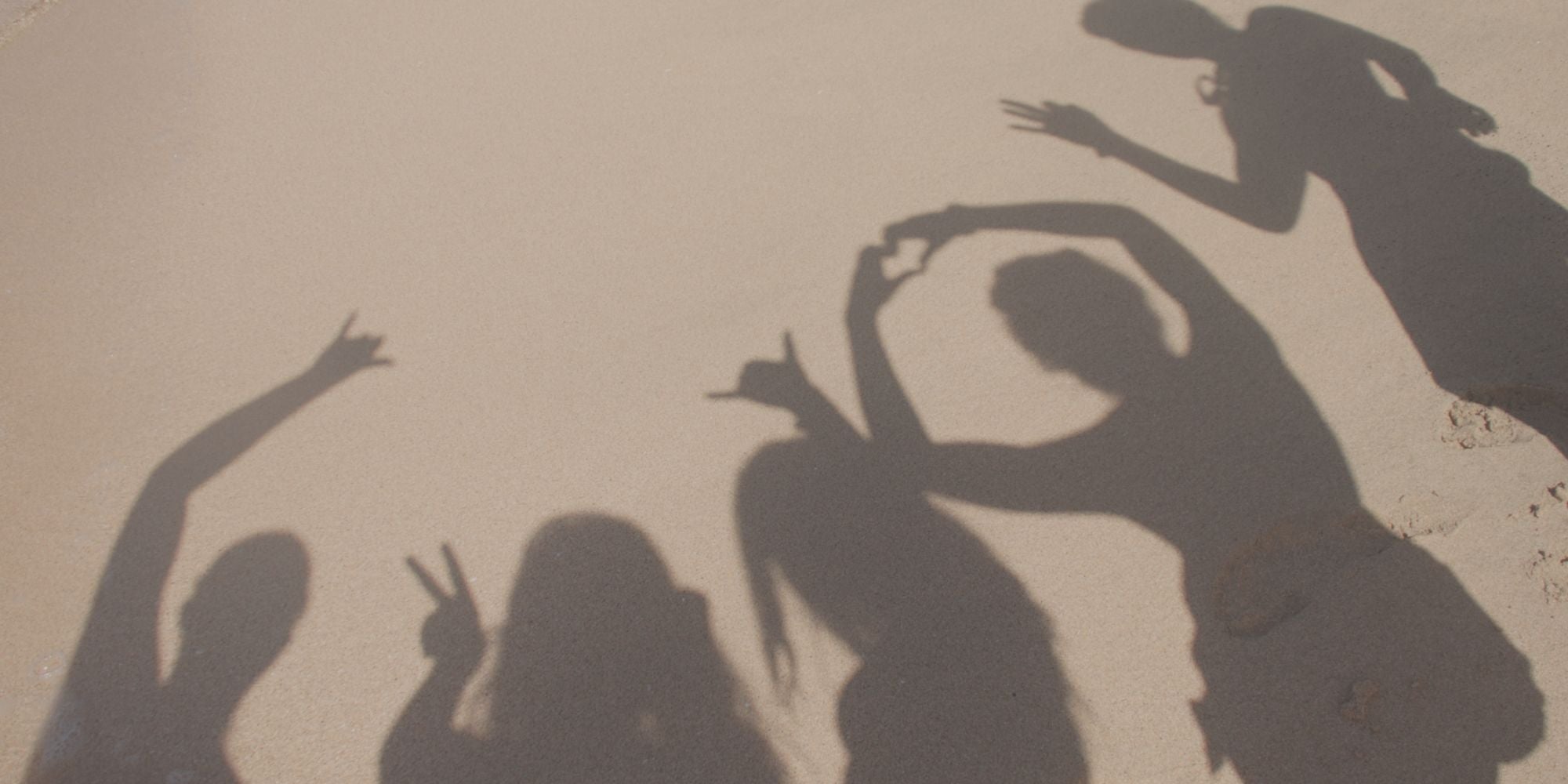 Shadows of friends making playful hand gestures on the beach, representing fun, friendship, connection, and joyful lifestyle moments.